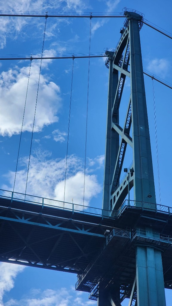 Looking up at a teal suspension bridge tower against a blue sky