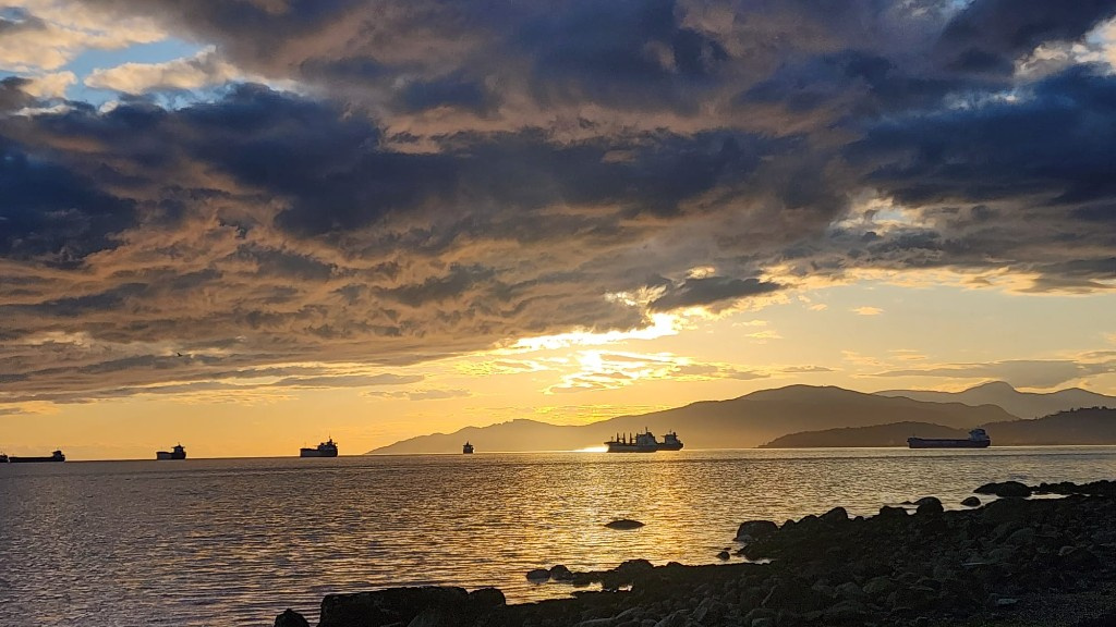 Golden sunset over the water with cargo ships and mountains
